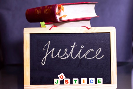 CHALKBOARD WITH JUSTICE WRITTEN ON IT WITH LAW BOOKS WITH A BLACK BACKGROUNDの写真素材