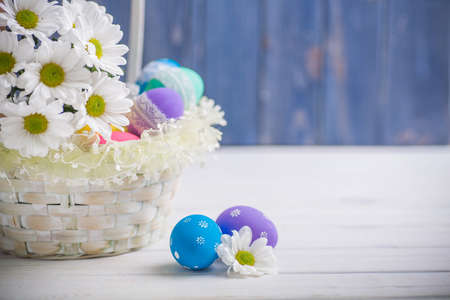 easter present basket with white flowers and colored eggs on white wooden background spring inspirationの写真素材