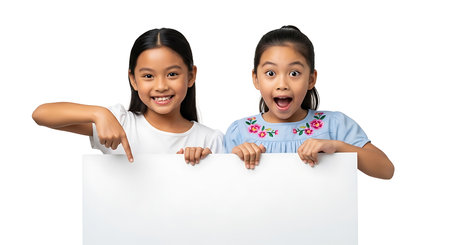 Two cheerful young girls with dark hair and bright smiles holding a blank white sign against a plain background, conveying excitement and surprise perfect for family or children marketing.の素材