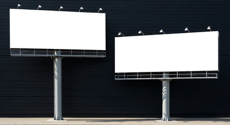 Two large blank billboards on tall metal poles stand in front of a dark industrial wall with horizontal lines, creating a modern and minimalistic urban scene suitable for advertising concepts.の素材