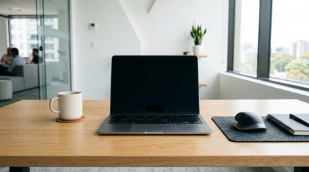 A modern office workspace with a laptop, coffee cup, and office supplies on a wooden desk, with a city view through the window.
