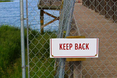 A keep back sign on a chain-link fence.