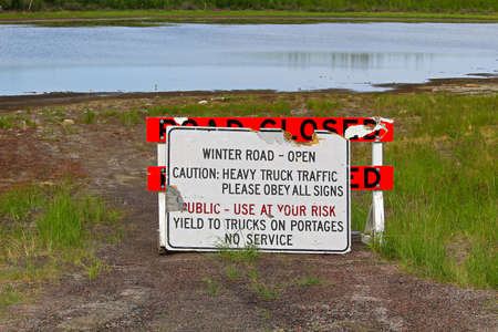 A road closed barricade and a winter road open sign leaning against each other.の写真素材