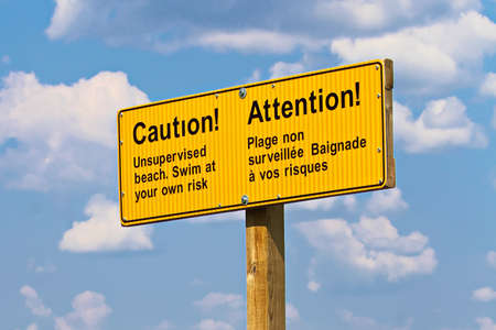 A yellow caution unsupervised beach sign in french and english.