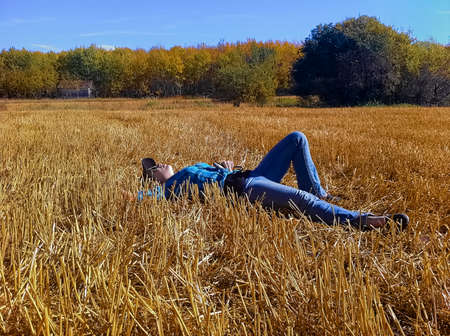 A young girl taking a break while working on a farm, laying down in a straw field looking up at the sky.の写真素材