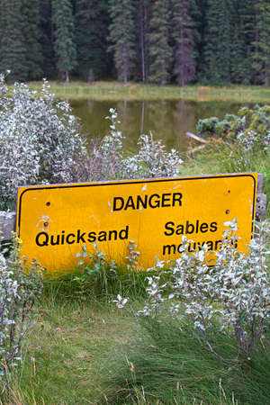 A danger quicksand sign with a pond in the background.