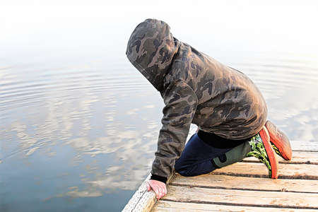 A child looking into water with a mirror reflection of the skyの写真素材