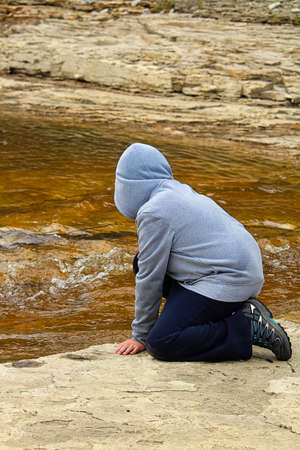 A young boy at a rivers edge watching water flowingの写真素材