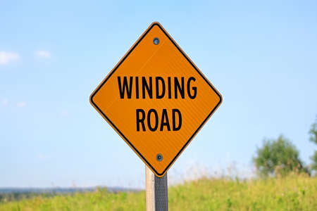 A winding road sign against a blue skyの写真素材