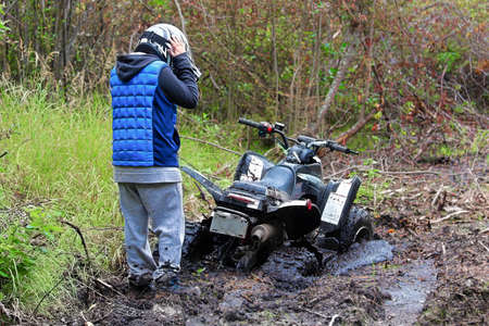 A young boys holds his helmet looking at his stuck quad.の写真素材
