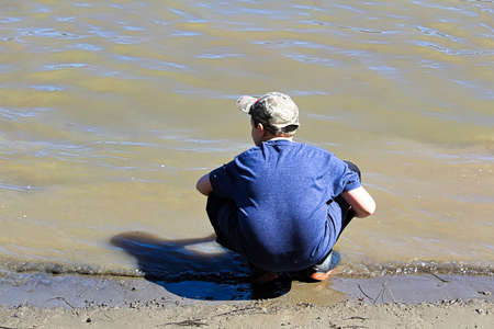 A young boy squats on the shore