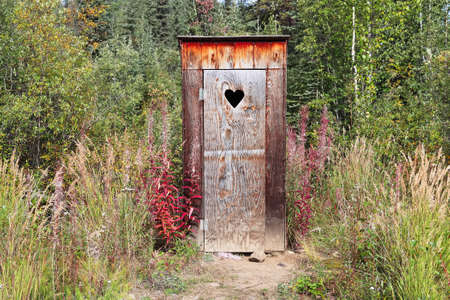 An outhouse in a wooded area with a heart windowの写真素材