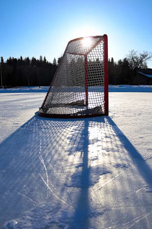 Sun silhouetting a empty hockey net on a frozen pond