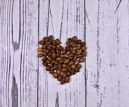 Coffee beans in heart shape isolated on wooden background. Espresso ingredients. Raw coffee beans....