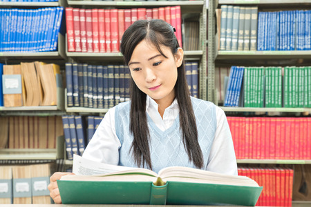 Asian student with open book reading it in college libraryの写真素材