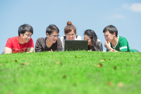 Group of students outdoors lying on grass and looking computerの写真素材