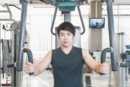 Asian man having fitness training in gym to build up muscle on a weight machine