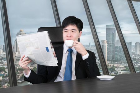 Businessman reading a newspaper while drinking coffee in his officeの写真素材