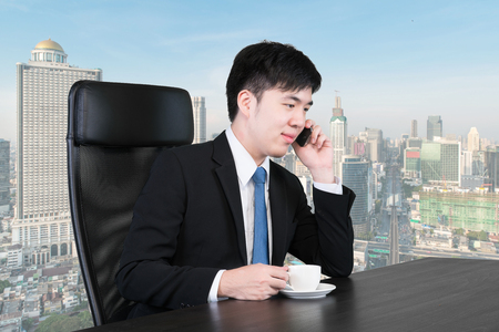 Asian businessman talking on the phone in high office buildingの写真素材