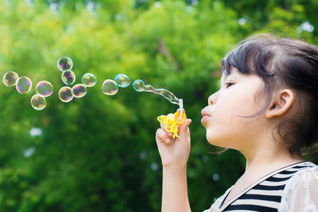Asian little girl blowing soap bubbles in green park
