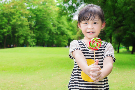 Asian little girl eating lollipop outdoors in spring parkの写真素材