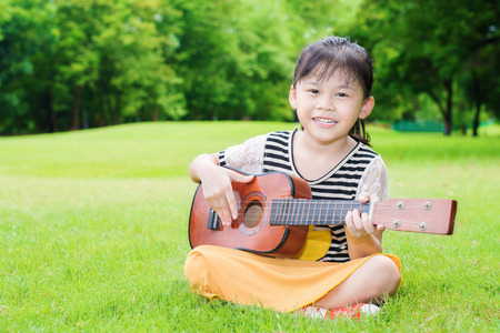 Asian little girl sitting on grass and play ukulele in parkの写真素材