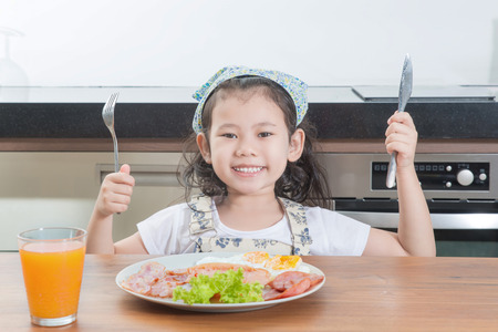 family, children and happy people concept - Asian girl child eating american breakfast in homeの写真素材
