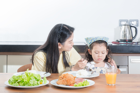 Asian girl kids with expression of disgust against eat rice while mother feed breakfastの写真素材