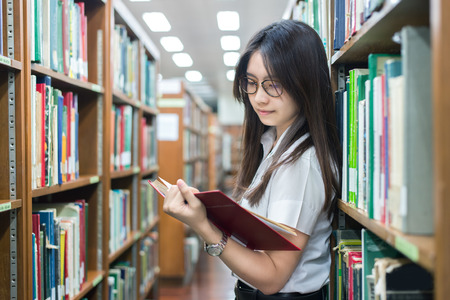 Asian student in uniform reading in the library at university