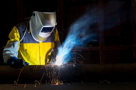 Worker with protective mask welding metal in factoryの写真素材