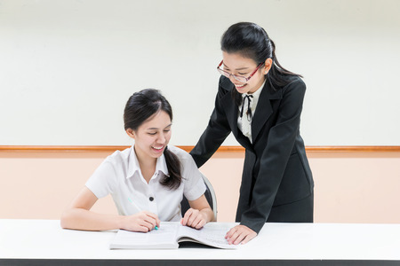 Teachers guide something to asian student in uniform at classroomの写真素材