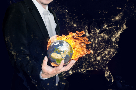 Business man holding the burning global earth in his hands against america city night light.Global warming and ecology concept.の写真素材