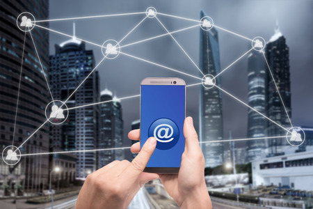 Hand holding smartphone and click on button with at sign linked with people icons. Email marketing,...