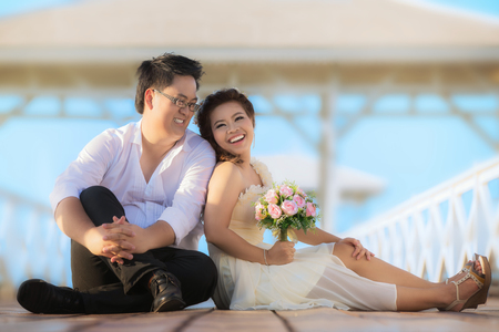 Portrait of cheerful wedding couple hugging and looking at the camera. Asian wedding couple in bridge near sea.の写真素材