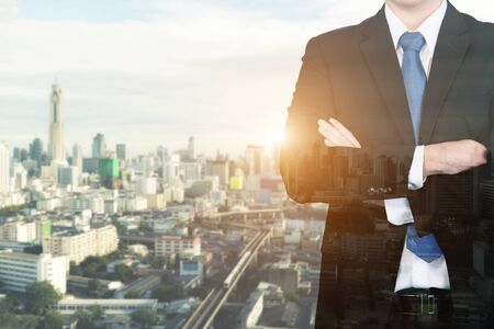 Double exposure businessman standing with his arms crossed against a city panorama. Toned image.の写真素材