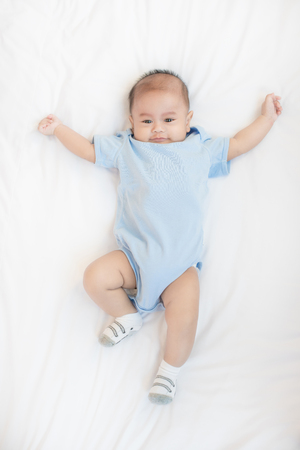 Portrait of 4 month Asian baby lying on white bed in bedroom at house, top view.の写真素材