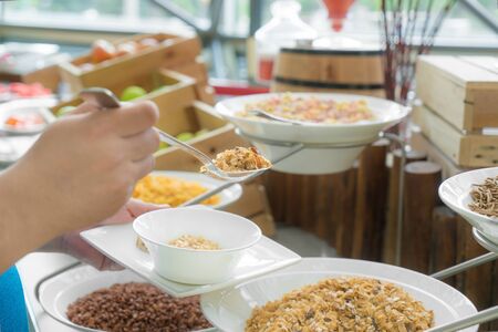 Hand spoon some kind of cereals on a self service breakfast in a hotel restaurant.の写真素材