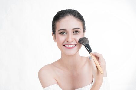 Asian Woman beauty ace Makeup. Portrait Of beautiful Asian young female applying foundation on face with cosmetic brush. Isolated on white backgroundの写真素材