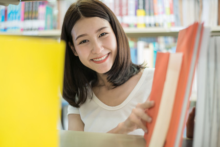 Portrait of an Asian college student seaching book for reseach in library.の写真素材