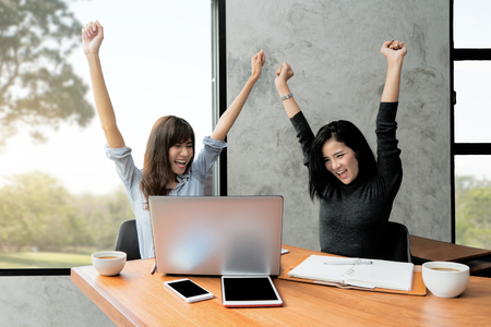 Happy excited successful Asian two business woman making arms up in office. Successful business team.の写真素材