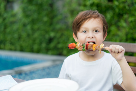 Cute little boy eating grilled barbecue in house.の写真素材