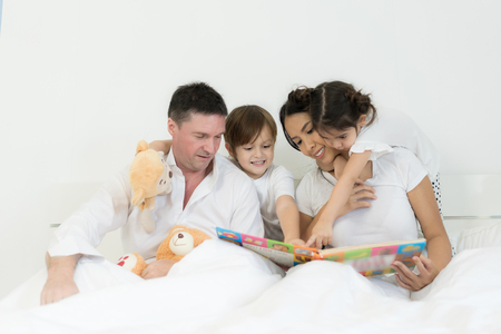 Asian brothers and Asian daughter reading book together on bed in bedroom with father and mother. Happy family concept.のeditorial素材