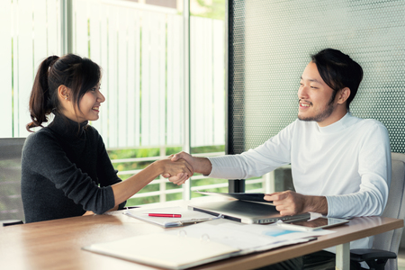 Couple of Asian business people with casual wear talking with happy and shaking hand in modern Office or coffee shop. Business sucess conceptの写真素材
