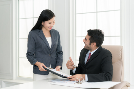 Asian businessman and his assistant Secretary in his office. The Secretary brought the boss documents to sign,Boss signs at documents and thumb up.の写真素材