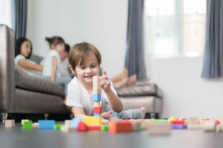 Asian boy playing wood toy in living room with father, mother and daughter in background. Happy family.の写真素材