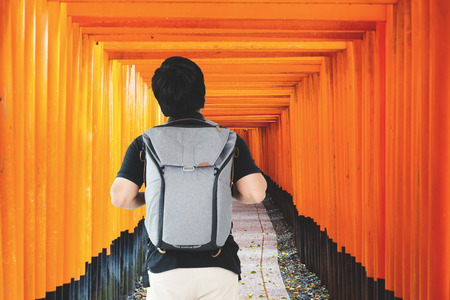 Asian traveler man with backpack standing at Red Tori Gate at Fushimi Inari Shrine in Kyoto, Japan.のeditorial素材
