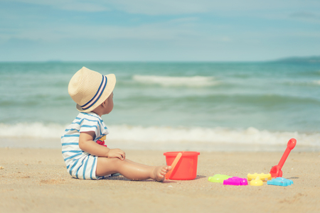 Asian 10 months baby boy playing on the sandy summer beach near the sea. Summer, Travel, Holiday concept.の写真素材