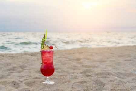 Red cocktail drink on sand in beach in twilight sea & sky background. Summer, Vacation, Travel and Holiday concept.の写真素材