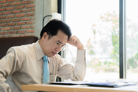 Asian businessman sitting and thinking in cafe, looking frustrated and depressed.の写真素材