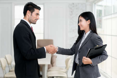 Successful job Asian businessman and businesswoman shaking hands in board room when finishing up a meeting.の写真素材